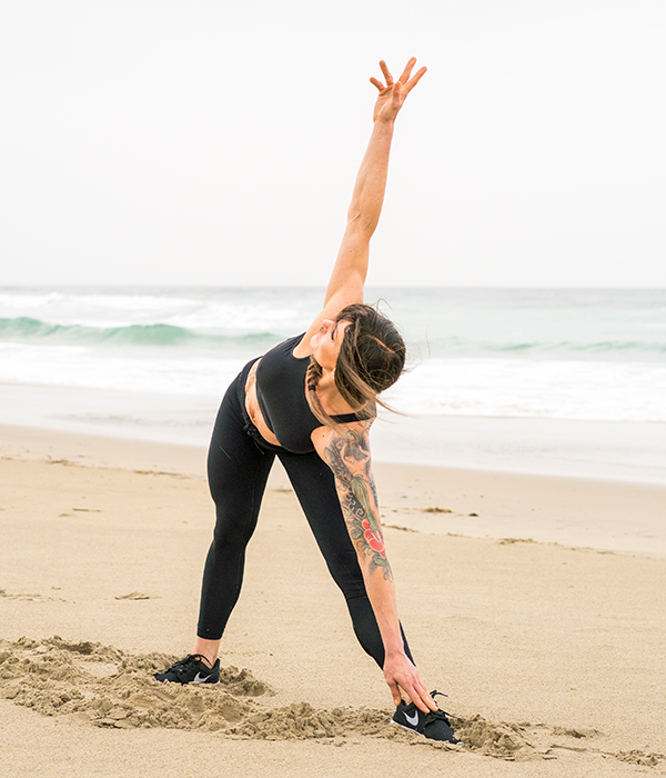 En kvinne med langt, mørk hår gjør yoga på stranden