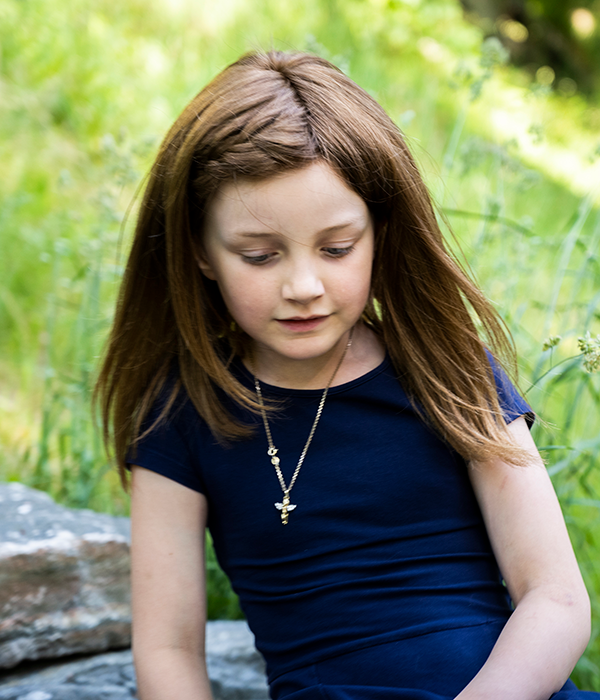 En ung jente med mørk parykk sitter på en gressplen